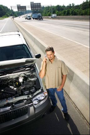 A man is talking on a cell phone next to a broken down car.