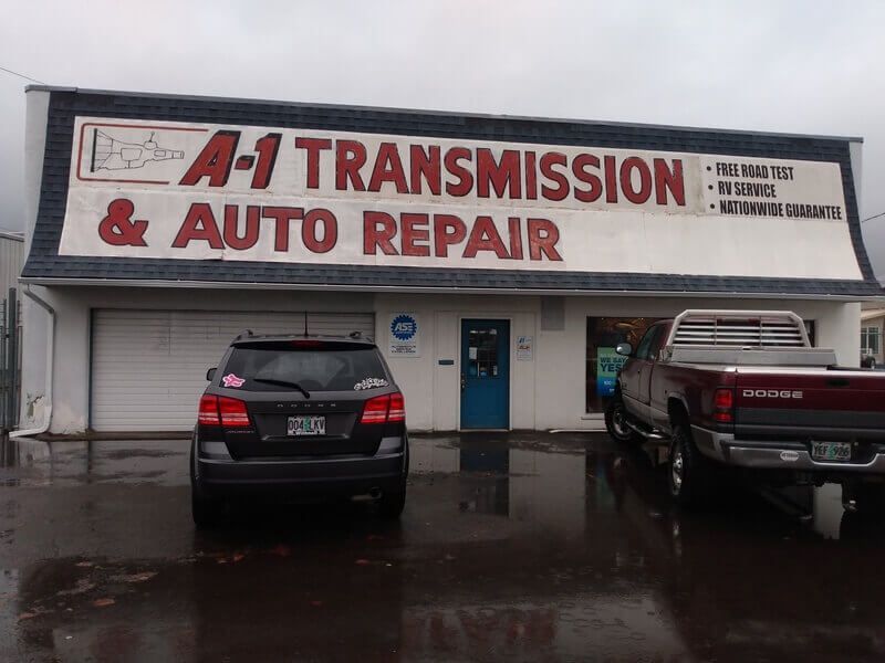Two cars are parked in front of a transmission and auto repair shop.