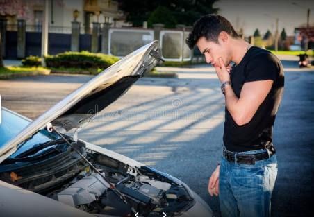 A man is looking under the hood of a broken down car.