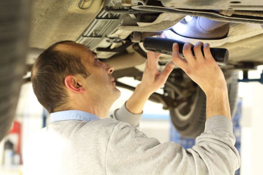 A man is looking under a car with a flashlight.