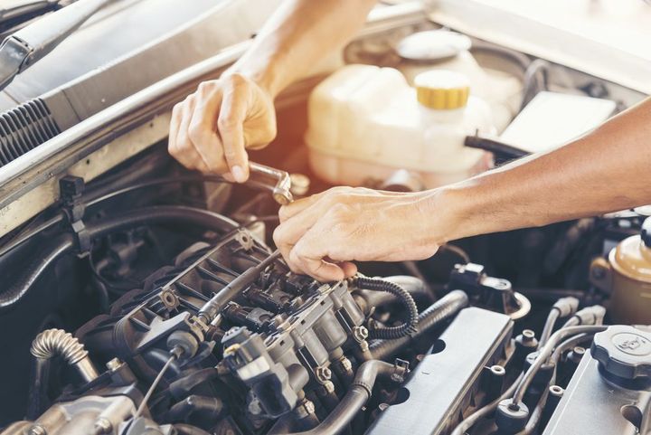 A man is working on the engine of a car with a wrench.