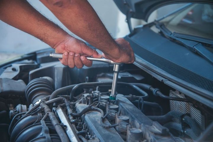 A man is working on the engine of a car with a wrench.