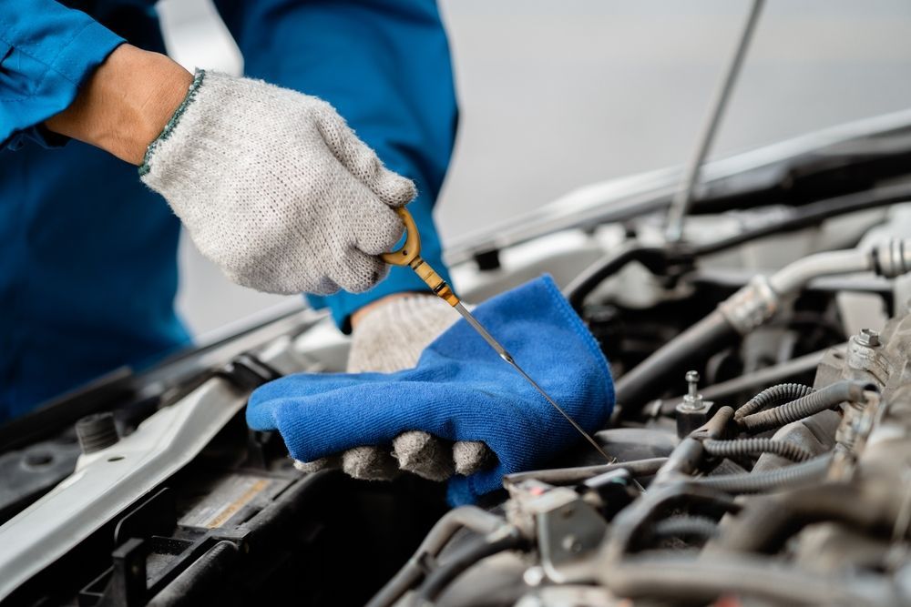 A mechanic is checking the oil level of a car with a dipstick.