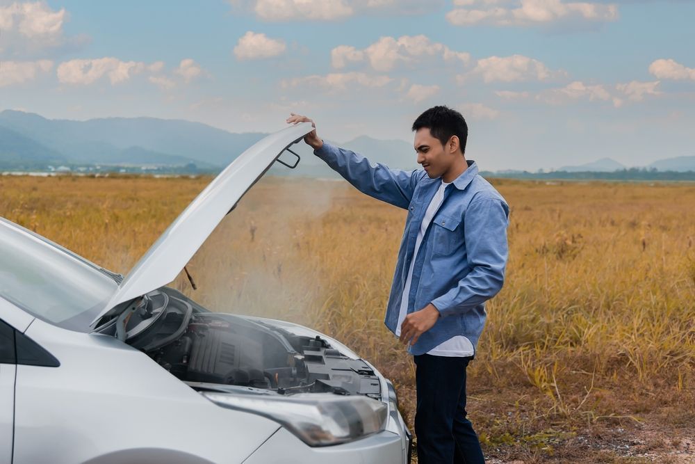 A man is looking under the hood of his broken down car.