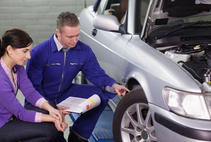 A man and a woman are looking at a car in a garage.