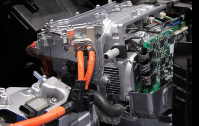 A close up of a car engine with orange wires coming out of it.