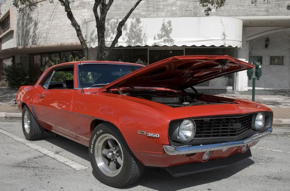 A red car with the hood up is parked in front of a building.