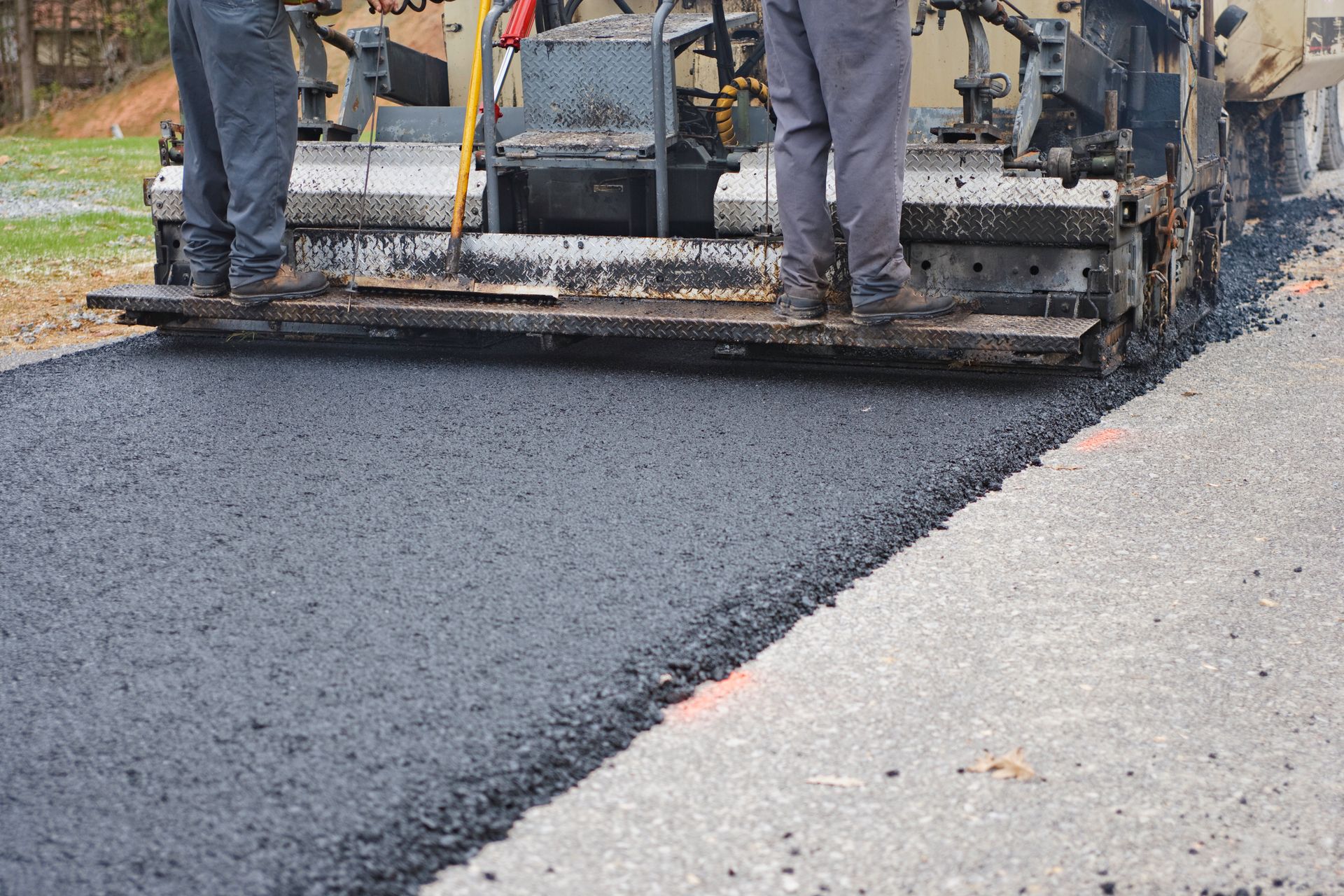 Asphalt paving machine laying blacktop on a road; workers standing on the machine.