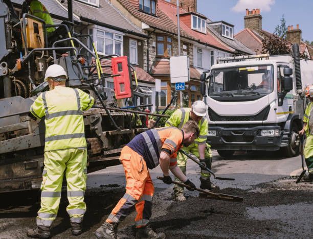 Road workers in reflective vests paving a street with machinery and a truck.