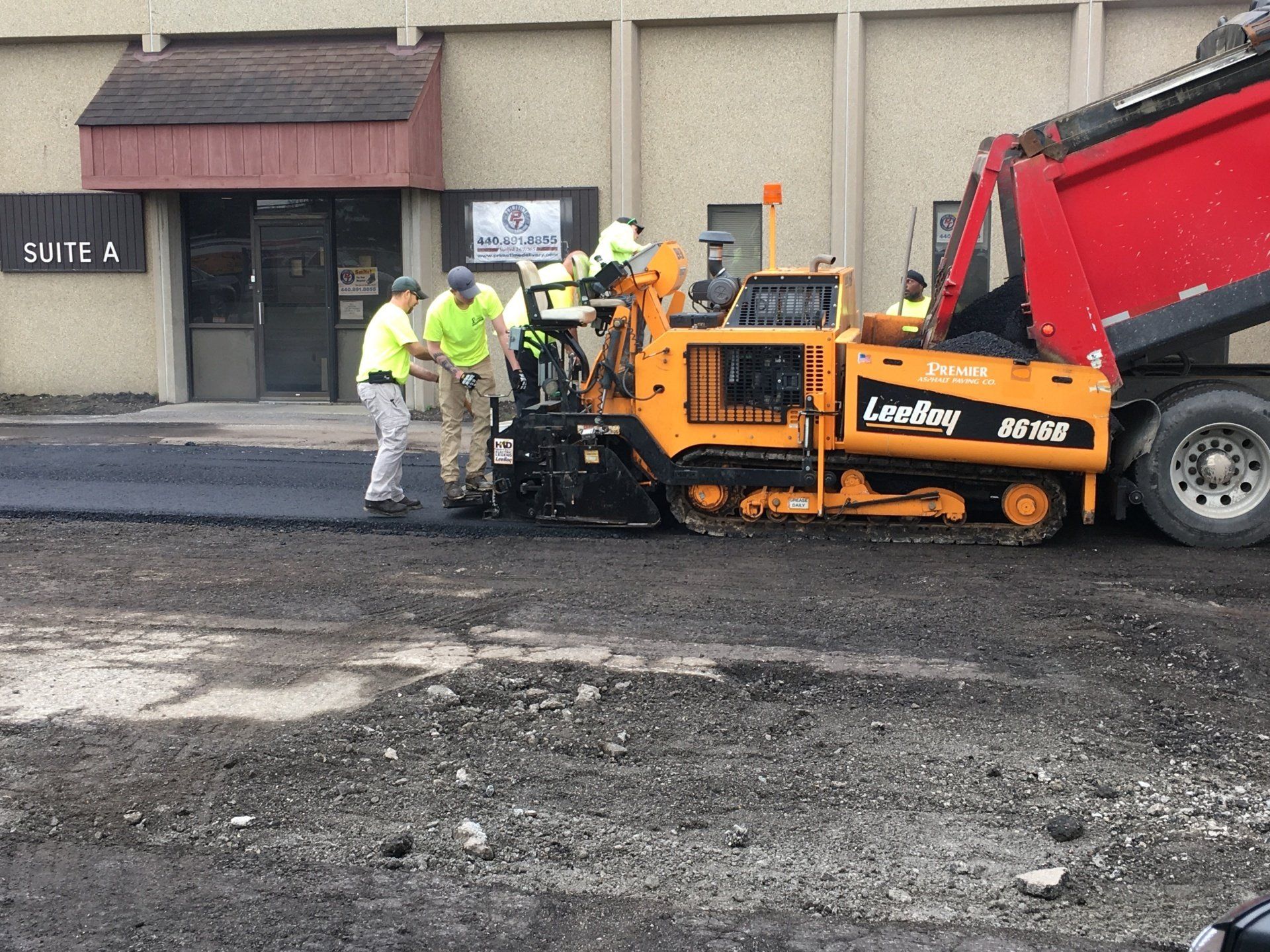 Road crew paving a parking lot with a yellow paver, dump truck, and workers.