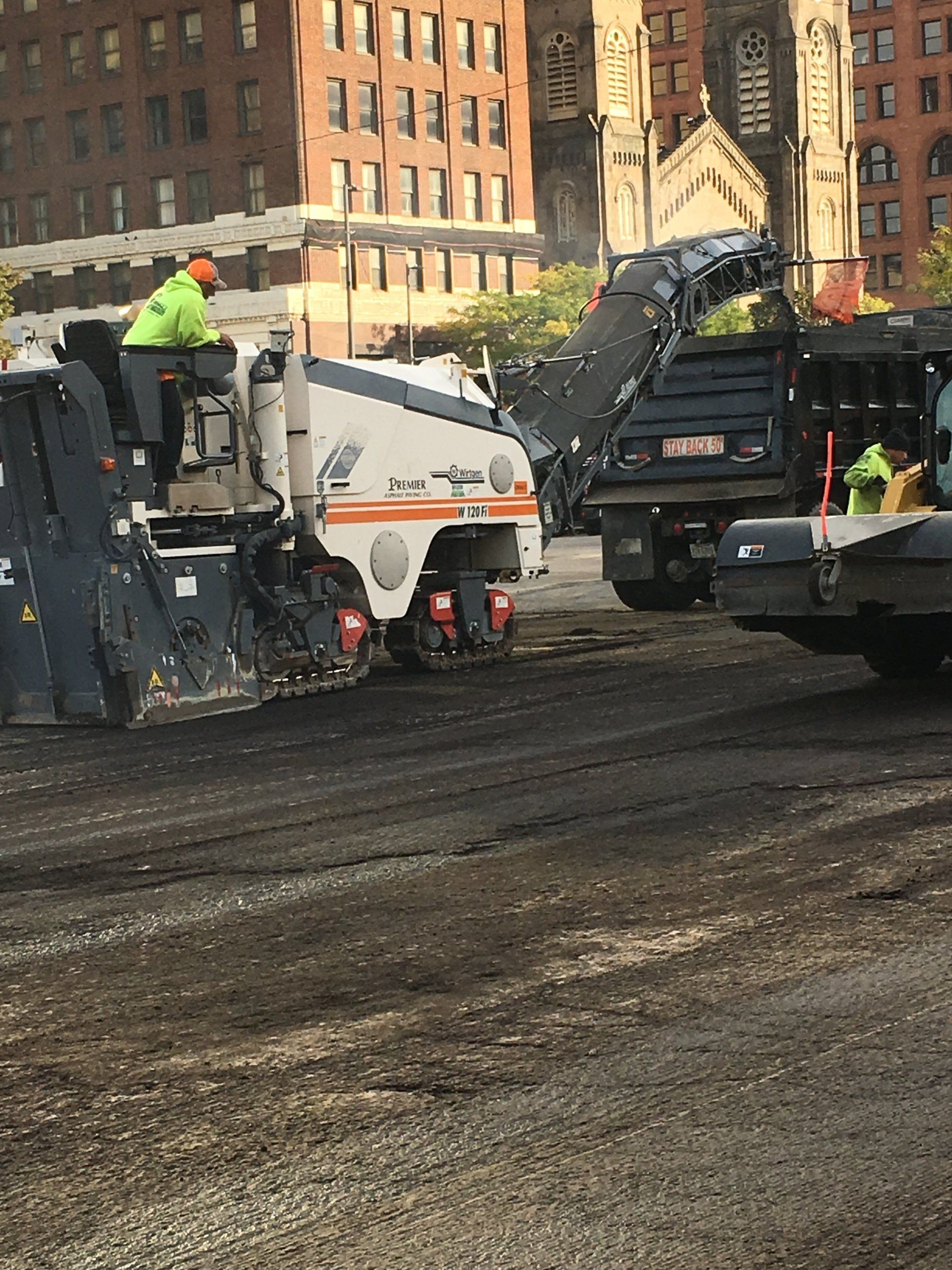 Asphalt milling machine removing pavement; construction workers in safety vests; urban setting.