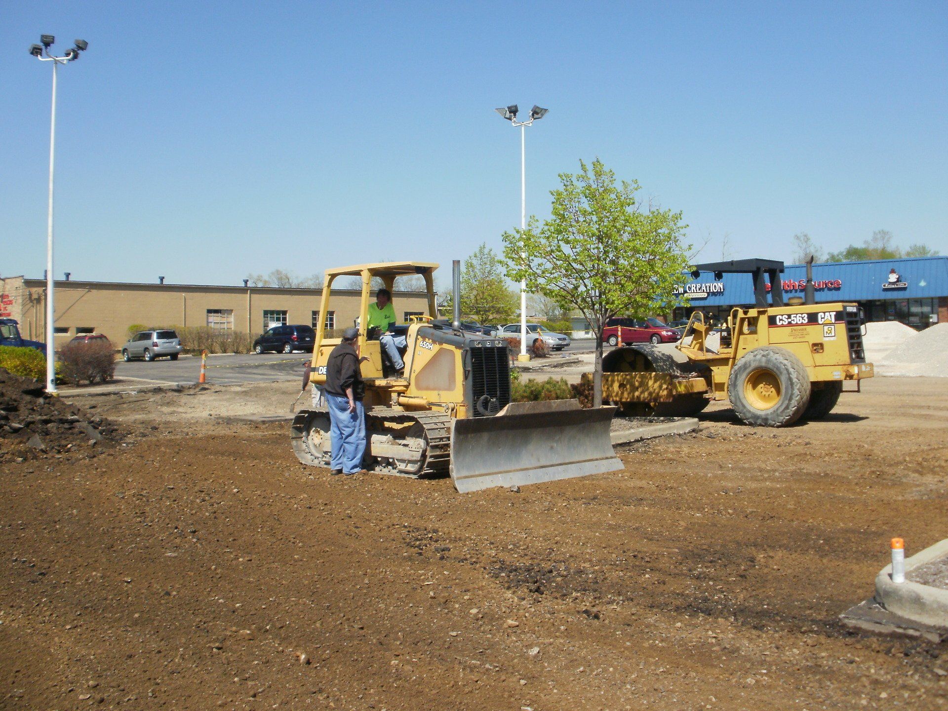 A small yellow bulldozer with a man talking to the driver on a dirt construction site.