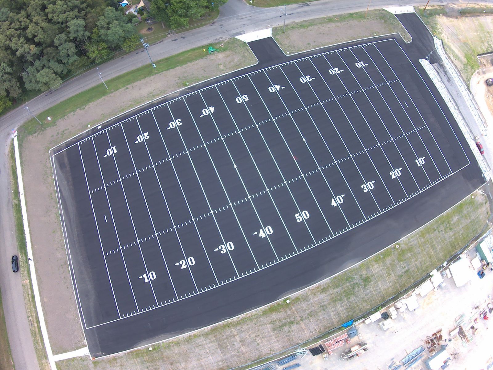 Aerial view of an empty black athletic field with white yard lines and surrounding track area.