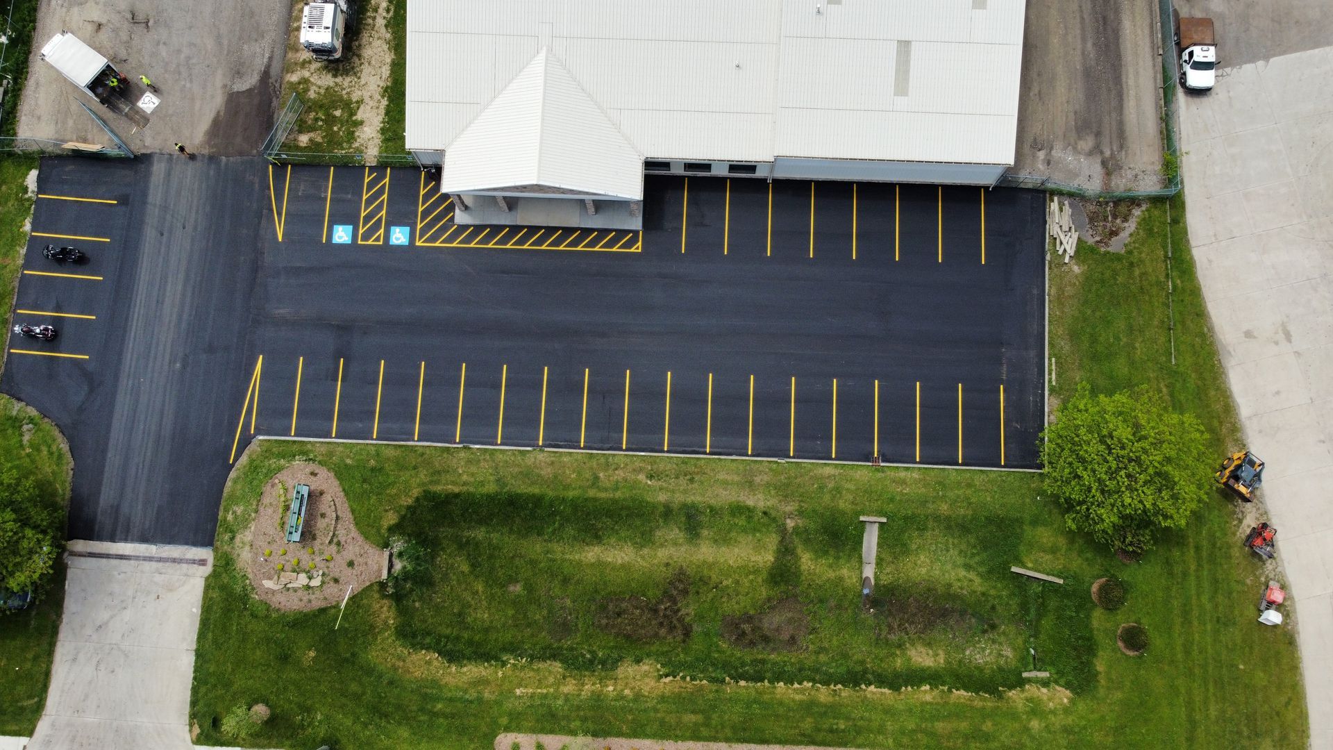 Aerial view of a parking lot beside a building, with yellow-lined spaces and a grassy landscaped area.
