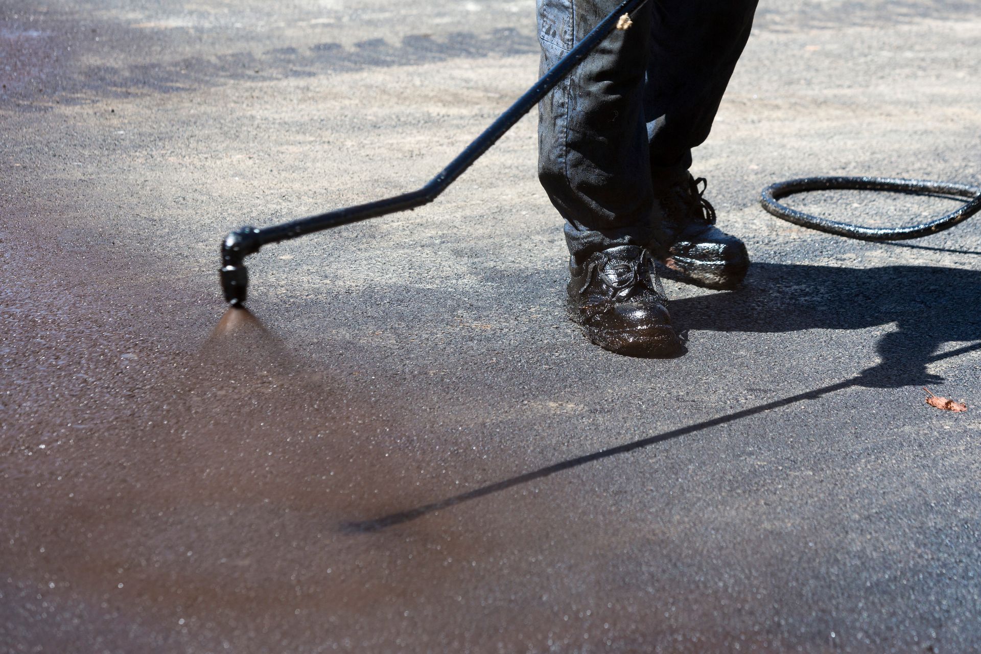 Worker spraying black hot asphalt at a road.
