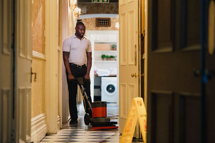 A woman is mopping the floor in a hallway next to a cart with buckets on it.