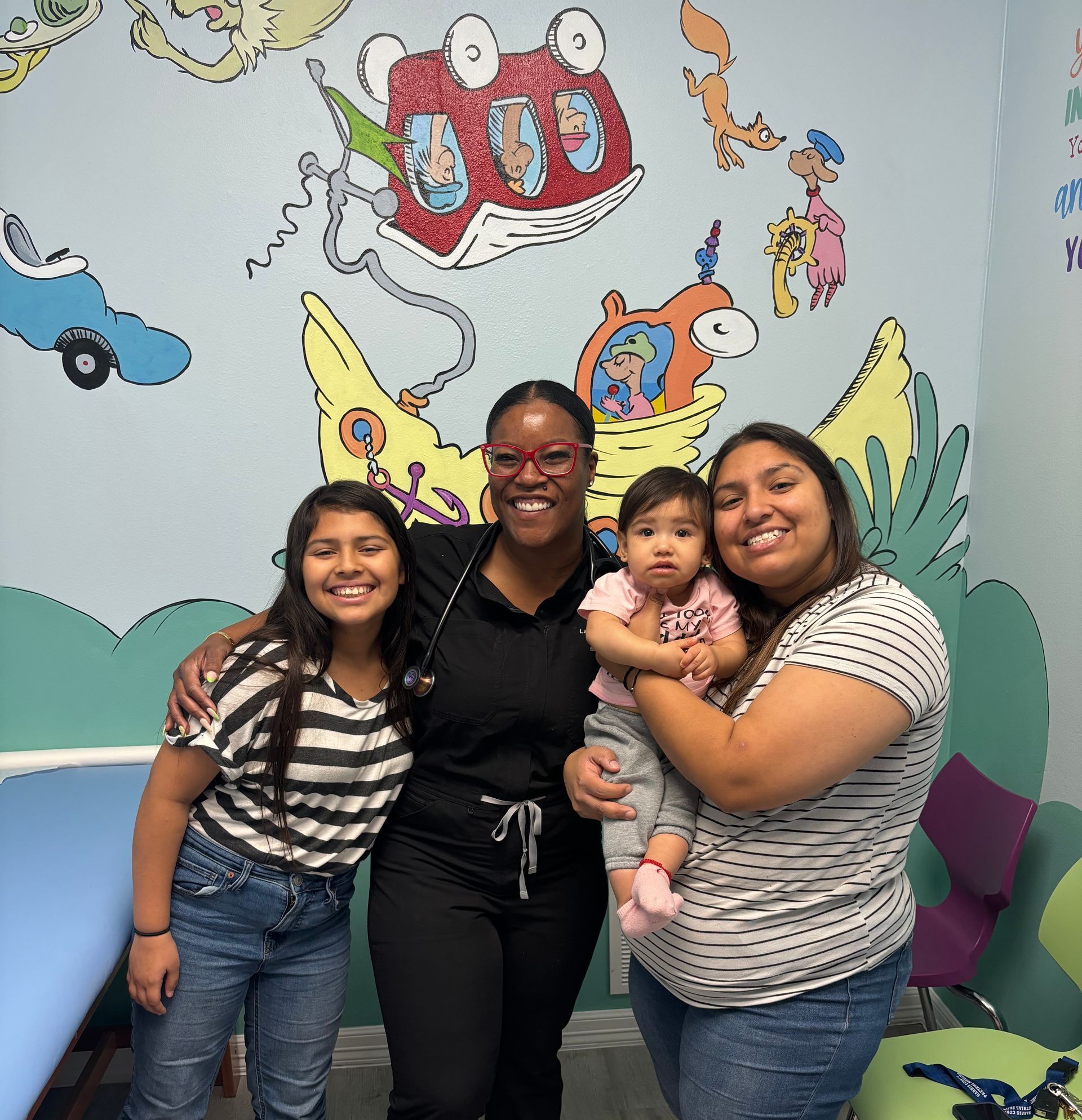 Four people pose in a Dr. Seuss themed room: a doctor, two mothers, and a baby.