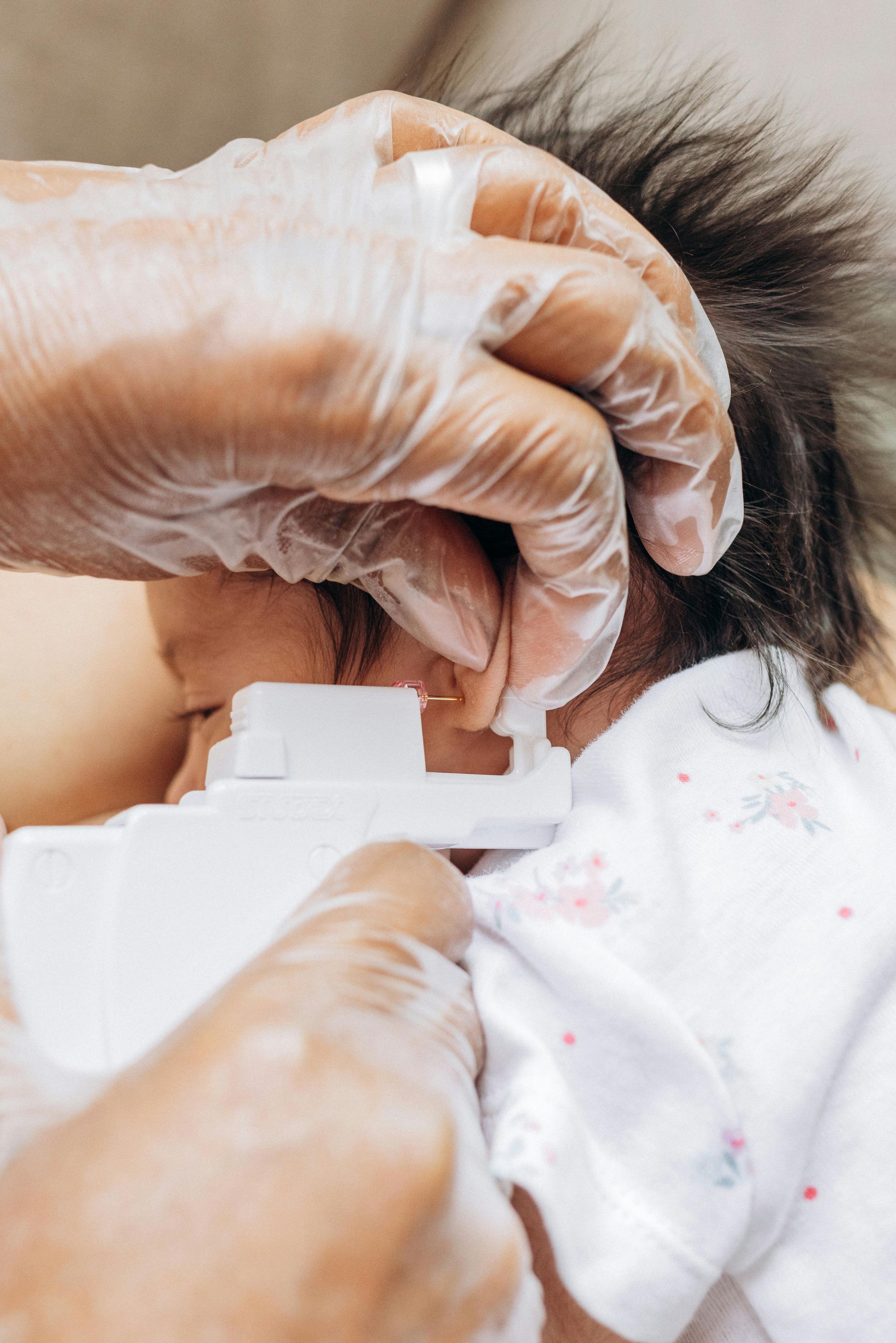 Person in gloves piercing a baby's ear.