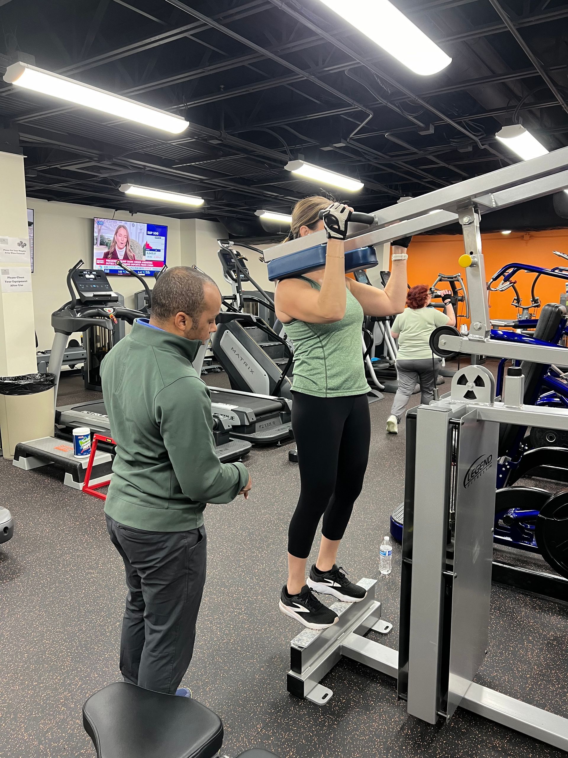 A man is helping a woman do a pull up in a gym.