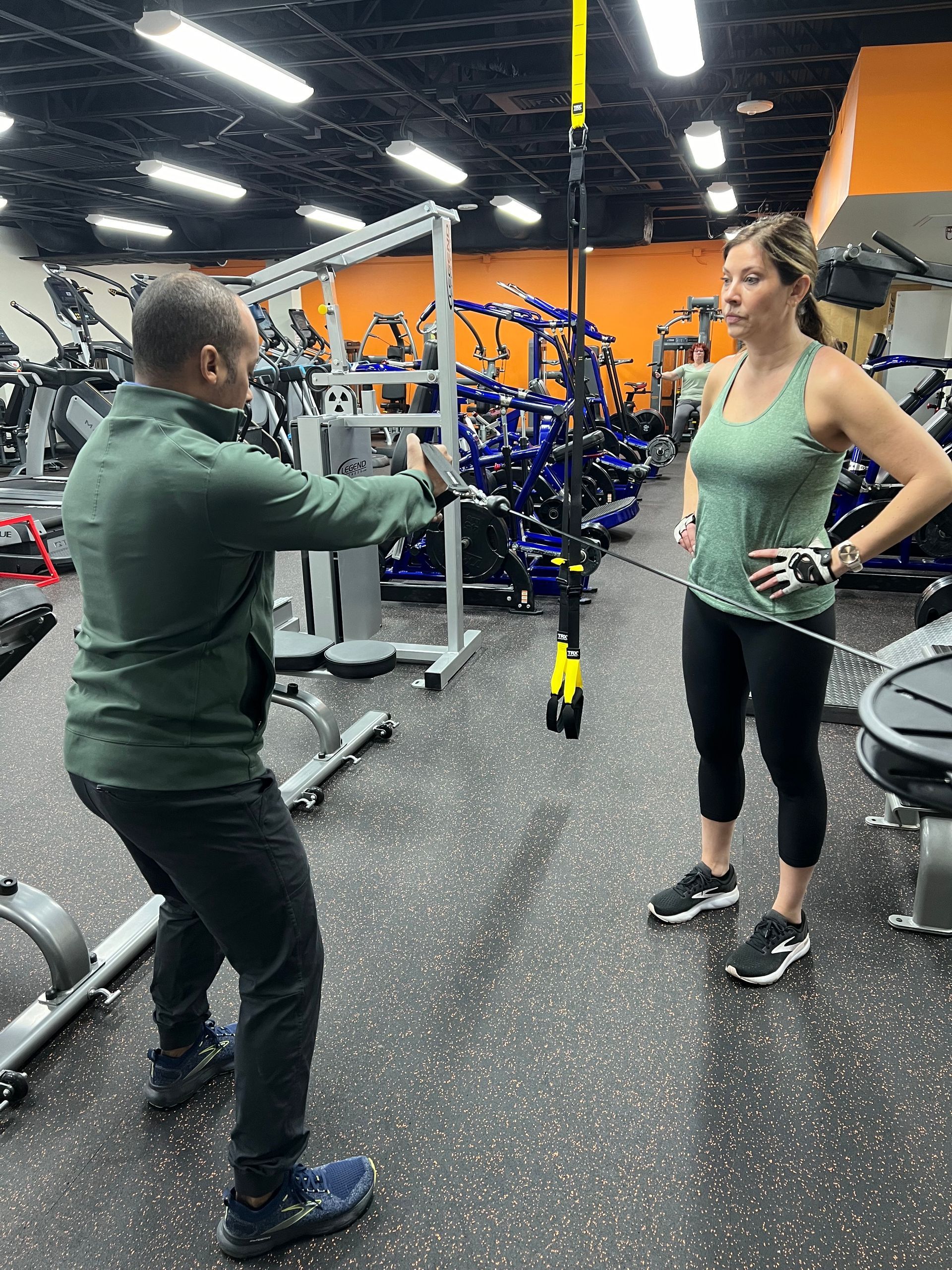 A man is teaching a woman how to use a machine in a gym.