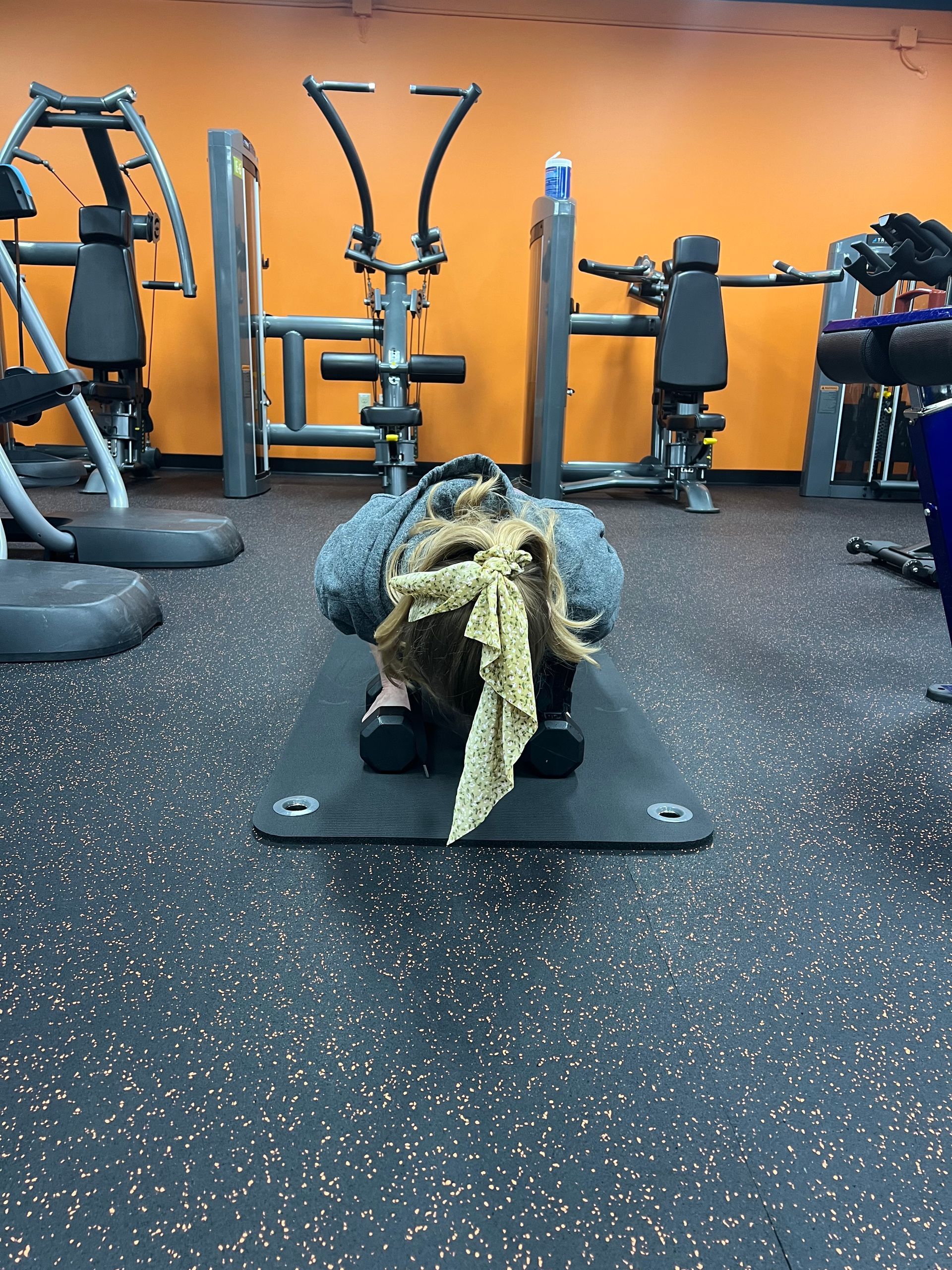 A person is laying on a mat in a gym with a towel around their head.