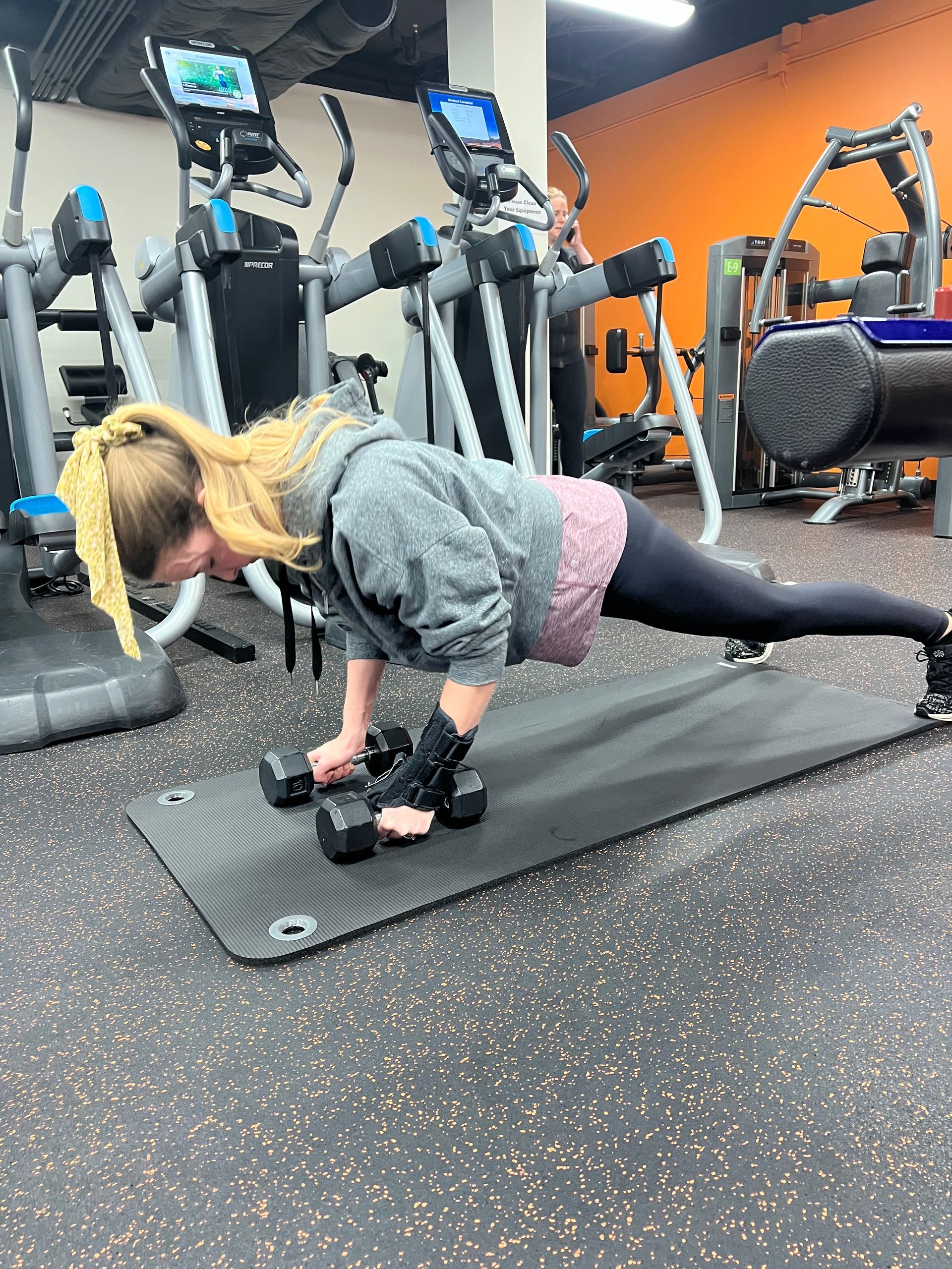 A woman is doing push ups with dumbbells in a gym.
