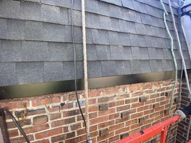 Brick wall with dark roof shingles above and a safety rope alongside.