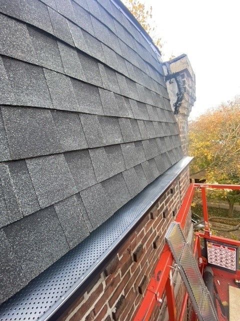Roof with dark gray shingles, a new gutter, and a red brick wall.