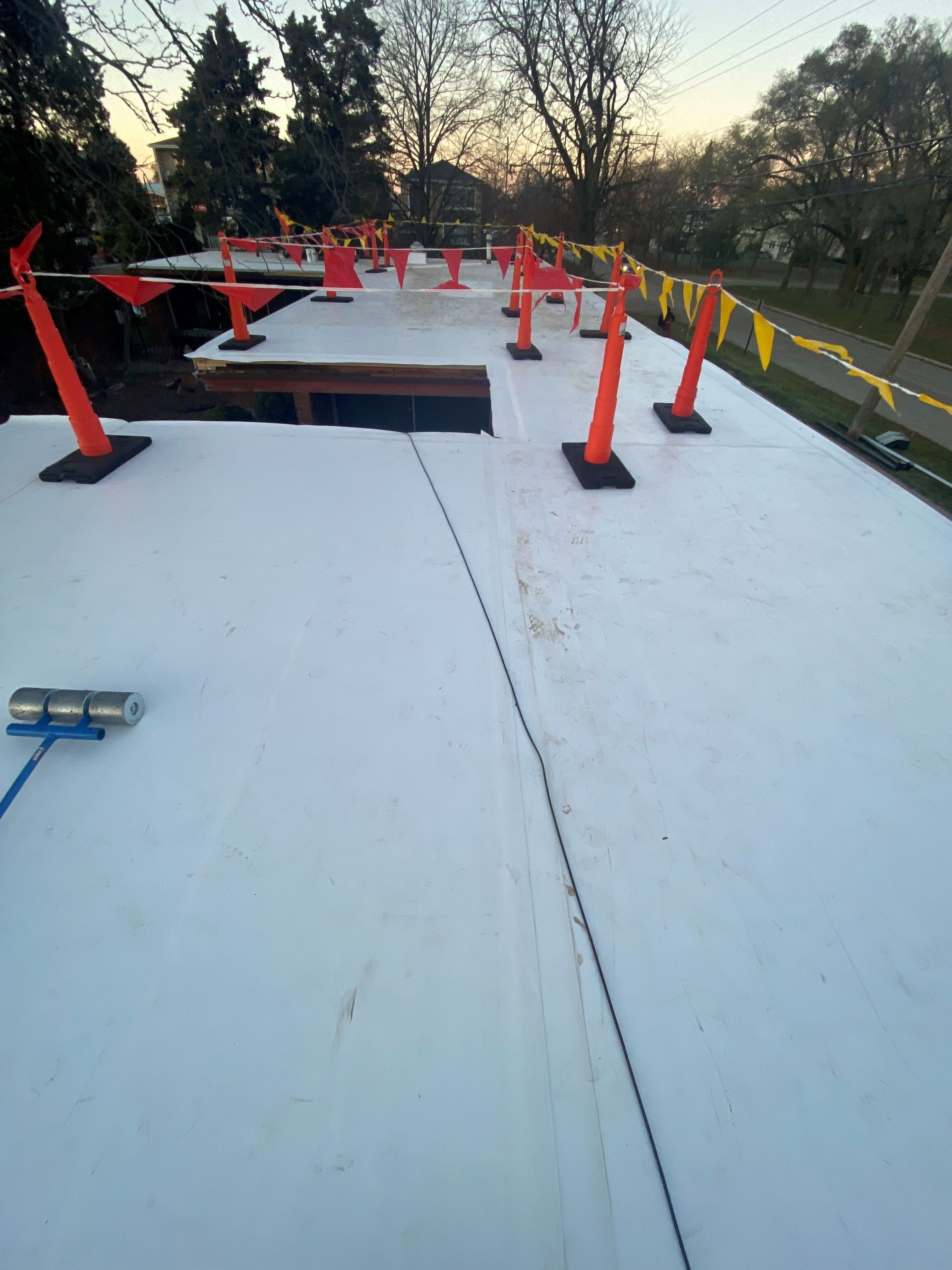 Rooftop with white surface marked by orange safety cones and banners; dusk setting.