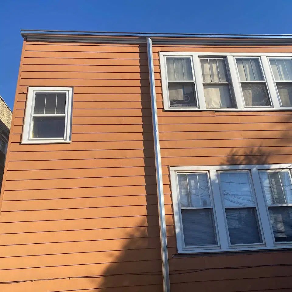 Two-story orange building with white-framed windows and a gutter against a clear, blue sky.