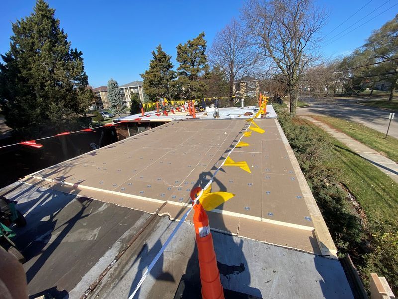 Rooftop work with safety flags; a flat roof with exposed layers. Daylight.