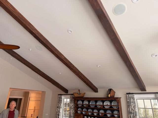 Angled ceiling with dark wooden beams. Recessed lights. Person in the corner. Cabinet with plates in background.