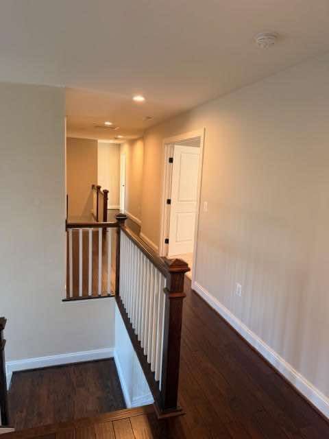 Hallway with hardwood floor, stairs, white doors, and a light tan wall.