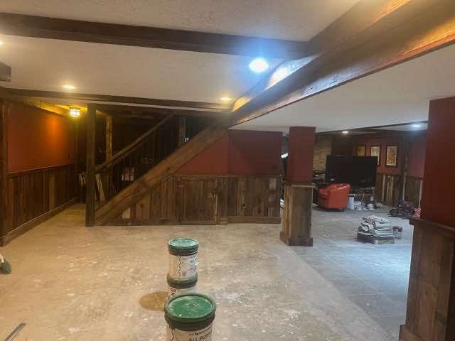 Basement under construction, with exposed beams and unfinished flooring. Paint cans in foreground.