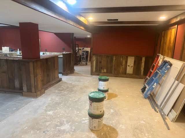 Basement under construction with rustic wood paneling, red walls, concrete floor, and building materials.