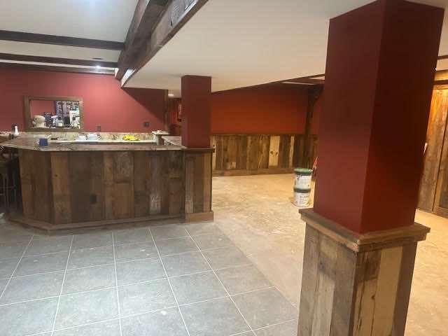Basement bar with rustic wood paneling, red walls, stone tile floor.