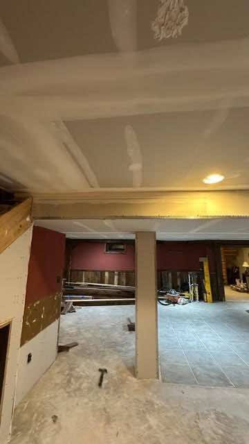 Interior under construction: drywall ceiling, exposed beams, unfinished floors, burgundy walls, a support column, and tools.