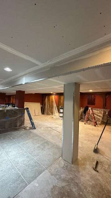 Basement undergoing renovation; drywall, support columns, and construction materials visible.