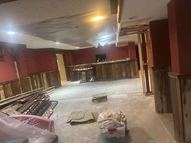 Basement remodel in progress. Wooden panel walls, red wall accents, and debris on the floor.