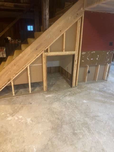 Wooden staircase under construction with framed storage space in basement. Concrete floor.