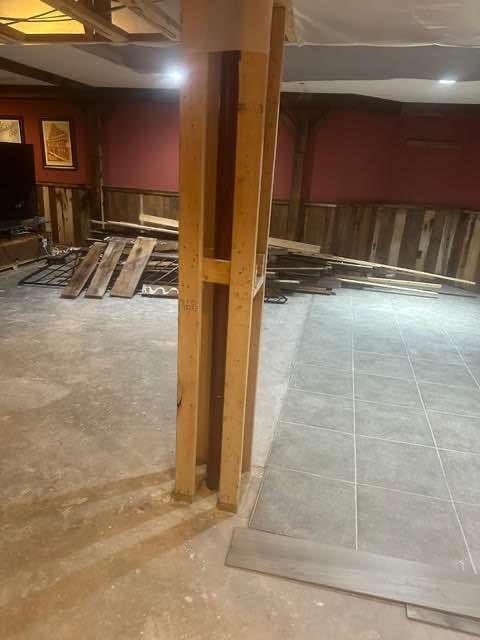 Basement undergoing renovation. Wooden support beam in the center, flooring and wall paneling are partially installed. Red walls.