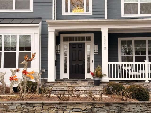 Front of a house with dark gray siding, white trim, and a black front door. Reindeer decorations on the lawn.