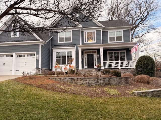 Blue two-story house with white trim, porch, and a lawn with some landscaping.