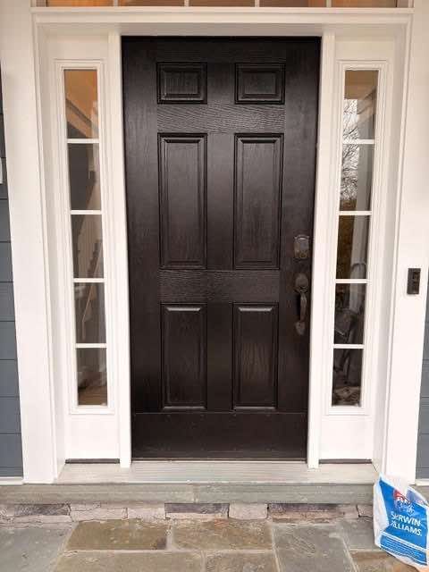 Black front door with sidelights, white trim, stone step.