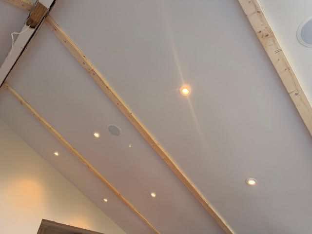 Angled white ceiling with recessed lights and wooden beams.