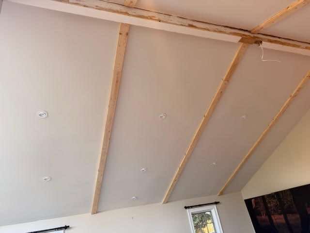 Angled, white ceiling with exposed wooden beams, recessed lights, and a window in the corner.