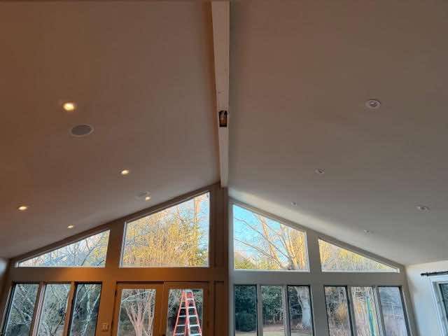 Interior of a room with high ceilings, windows, and recessed lighting. A beam runs across the ceiling.