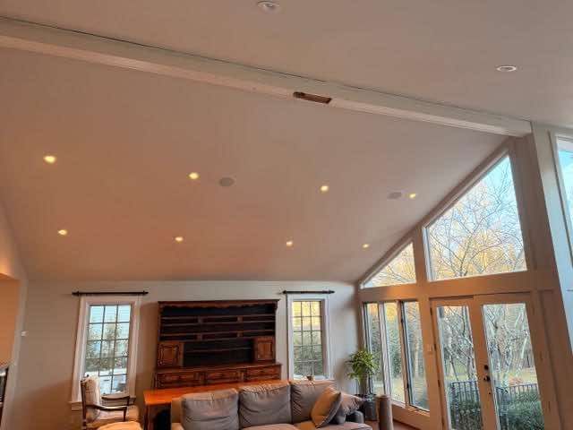 Living room with high ceilings, recessed lights, large windows, and a dark wooden cabinet.