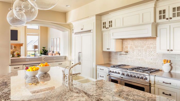 Elegant, white kitchen with marble countertops, stainless steel appliances, and hanging globe lights.