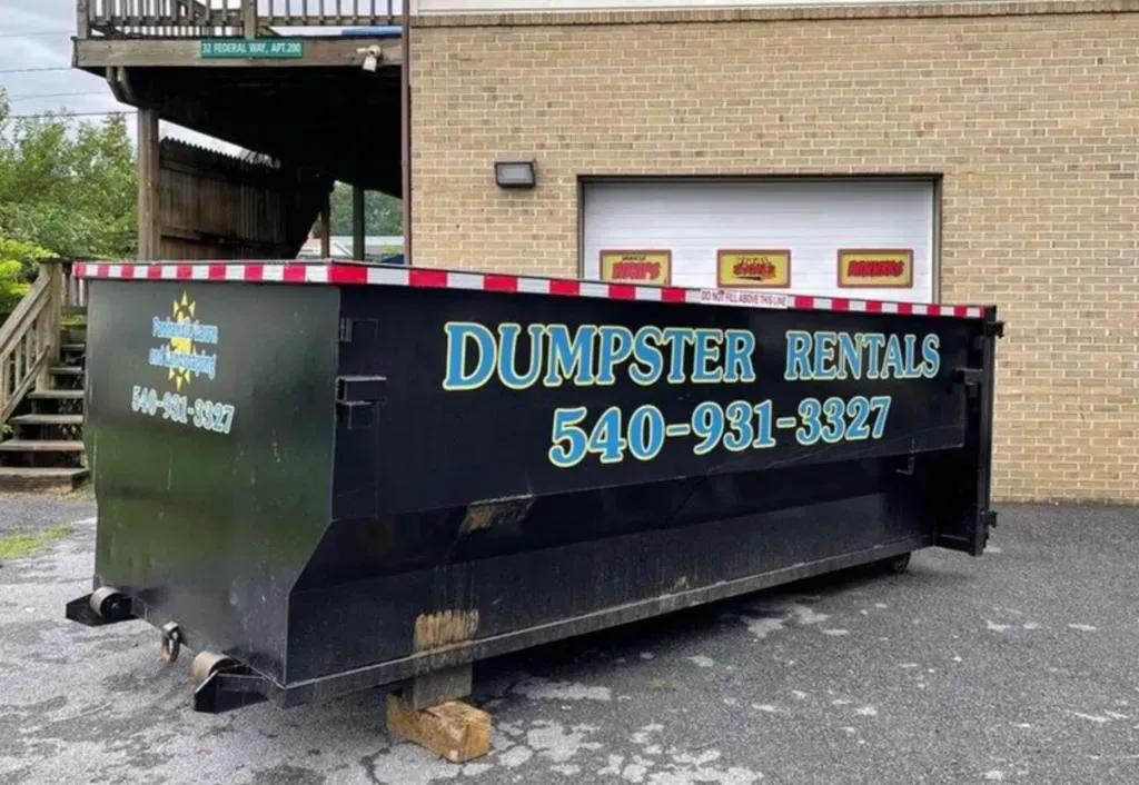 A dumpster is parked in front of a brick building.